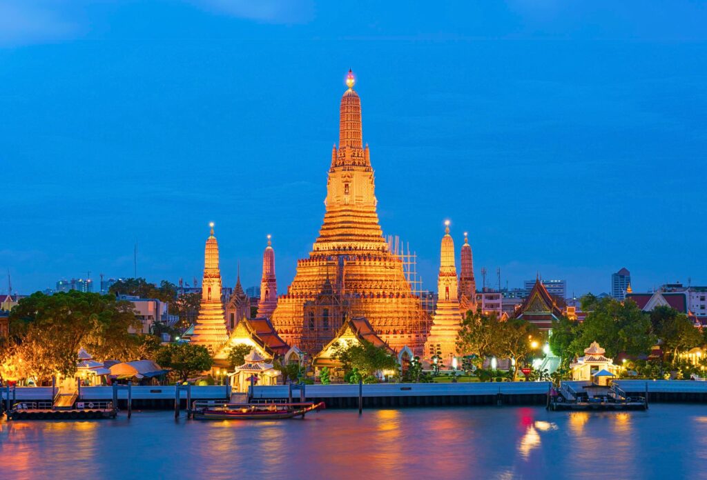 Templo Wat Arun iluminado ao entardecer às margens do rio Chao Phraya em Bangkok, um dos monumentos mais icônicos da Tailândia
